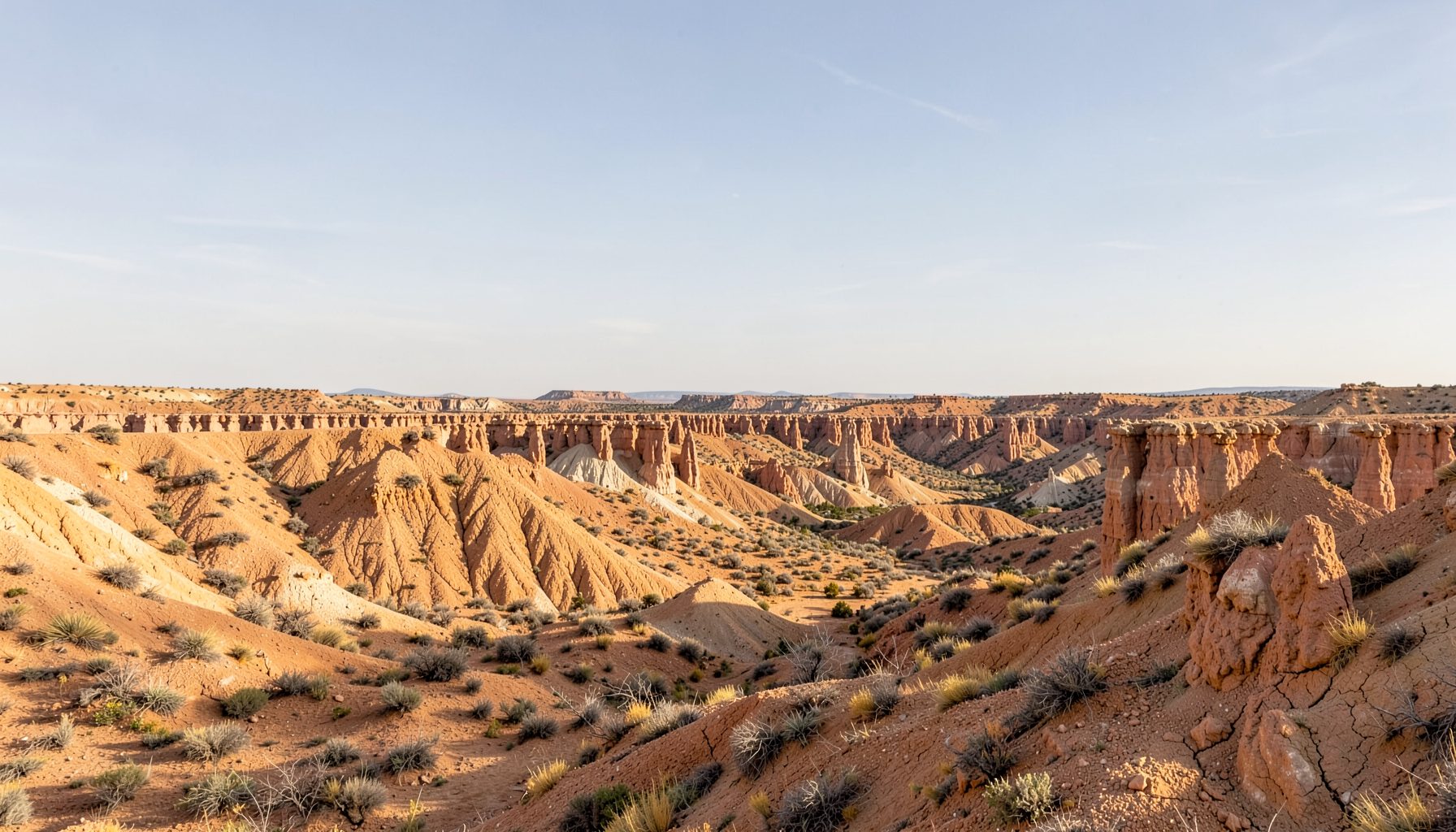 Badlands terrain in warm ochre and tan tones under a wide sky, with eroded hoodoo formations stretching toward the horizon, suggesting the Drumheller landscape.