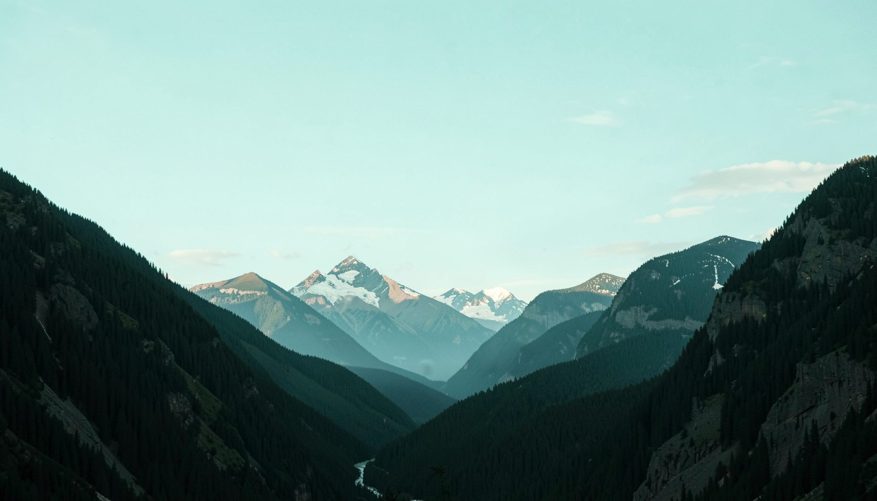 A wide horizontal photograph of mountain scenery near Banff with pale turquoise sky, dark evergreen slopes, and a soft muted mood